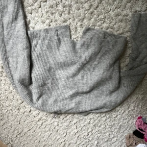 Grå stickad kofta med rosettknäppning - Superfin grå stickad kofta med långa ärmar och snygga rosetter som knäppning framtill. Koftan har en ribbad struktur och är perfekt för lager-på-lager under kyliga dagar. Enkel att styla och ger en mysig vibe till din outfit.