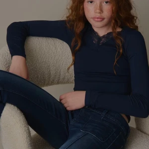 Mörkblå långärmad topp med spets - Mörkblå långärmad topp med v-ringning och snygg spetsdetalj vid halsen. Toppens passform är tight och materialet känns mjukt och stretchigt, troligen polyester eller bomullsmix. Perfekt att styla med jeans eller kjol för en clean look. Skriv gärna vid frågor!🤗