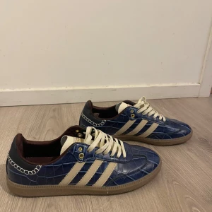 Adidas Samba blå croc sneakers - Unika Adidas Samba sneakers i blått croc-mönstrat skinn med klassiska vita stripes och beige sula. Skorna har vita snören, guldiga detaljer och mörkbrunt foder. Perfekt för dig som vill sticka ut med en retrovibe och cool textur.