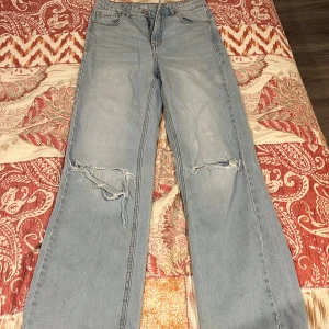 Ljusblå wide jeans från KappAhl  - Ljusblå jeans från KappAhl i wide fit med slitna detaljer över knäna. Klassisk femficksmodell med hög midja och raka ben. Tillverkade i hållbar denim för en cool och avslappnad look.