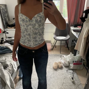 Blommig topp - Blommig korsetttopp i färgen vit och blå färg. Köpt på vinted men har aldrig kommit till användning, inga defekter, mycket bra skick. Kontakta mig vid frågor 💕☺️