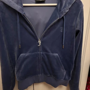 Blå velour hoodie från Juicy Couture - Säljer en blå velour hoodie från Juicy Couture med dragkedja och huva. Tröjan har en snygg J-detalj på dragkedjan, broderad logga på bröstet.
