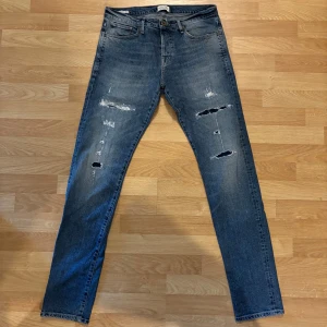 Jeans från Jack & Jones  - Säljer ett par snygga jeans från Jack & Jones med snygga slitningar. Storlek W31 L34. Modellen är 186cm och väger ungefär 70kg