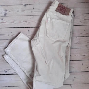 Levi's 501 vita jeans W32 L30 - Säljer ett par klassiska Levi's 501 jeans i vit färg. Modellen har rak passform, fem fickor och knappgylf. Jeansen är tillverkade i bomull och har den ikoniska läderpatchen bak i midjan. Perfekt för dig som gillar clean och tidlös stil.