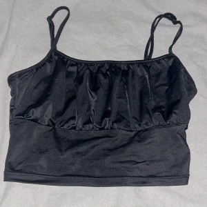 Svart linnetopp  - Svart linnetopp från H&M i storlek S. Toppen har smala axelband och ett rynkat parti framtill. Materialet är mjukt och har en lätt glansig finish, perfekt för att lyfta din outfit💕