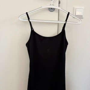 Svart ärmlös klänning med smala band - En stilren svart klänning med smala axelband och tajt passform. Perfekt för dig som gillar en clean look.