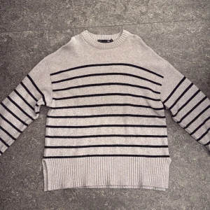 Grå randig stickad tröja 157 - Säljer en grå stickad tröja från 157 i storlek M. Tröjan har svarta horisontella ränder, rund halsringning och bred ribbad mudd nertill och vid ärmslut. Perfekt för lager-på-lager och chill dagar.