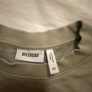 Mörkgrön sweatshirt från Weekday XS - En stilren mörkgrön  sweatshirt från Weekday i storlek XS. Tröjan har rund halsringning, ribbade muddar vid ärmslut och nederkant samt en klassisk, avslappnad passform. Perfekt för lager-på-lager och enkel att matcha med jeans eller kjol.