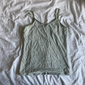Ljusgrön och vit randig linnetopp - Säljer en söt ljusgrön och vit randig linnetopp med smala axelband och v-ringad hals. Toppen har en enkel, rak passform. Kan sovas i eller annars passar den jättebra till jeans eller kjol!