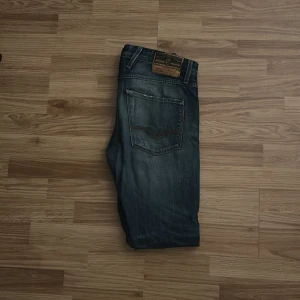 Replay Anbass jeans i mörkblå denim - Säljer ett par Replay Anbass jeans i mörkblå tvätt med snygga slitningar och klassiska fem fickor. Jeansen har smal passform. Märkespatch bak i midjan och diskreta detaljer på bakfickorna. Använt skick men en liten slitning på låret