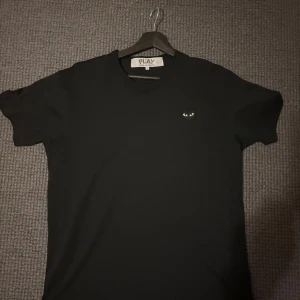Svart Comme des Garçons Play t-shirt - Svart t-shirt från Comme des Garçons Play med det ikoniska hjärta med ögon broderat på bröstet. Den är såklart äkta och den är införskaffad i USA. Säljer nu för att försöka iallafall få tillbaka lite pengar. Klassisk passform, rund hals och korta ärmar. Tillverkad i mjuk bomull som känns skön mot huden. Perfekt för dig som gillar stilrena och trendiga plagg.