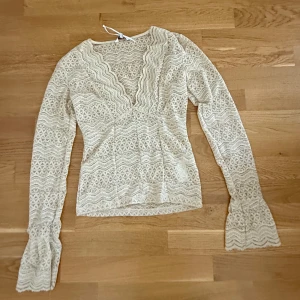Beige spetsblus från Bubbleroom XS - Supersöt beige spetsblus från Bubbleroom i storlek XS. Blusen har v-ringning, långa ärmar med volang vid ärmslut och ett detaljerat spetsmönster över hela toppen. Perfekt för dig som gillar romantiska vibes och snygga detaljer.