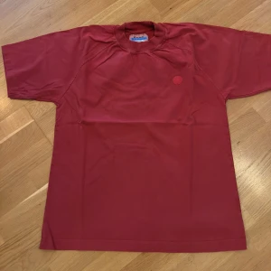 Röd t-shirt från Acne Studios Blå Konst - Snygg röd t-shirt från Acne Studios Blå Konst med rund hals och diskret logga på bröstet. Tillverkad i 100% bomull för en skön och avslappnad känsla. Perfekt basic med stilren design och normal passform.