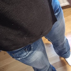 Blå bootcut jeans från Pepe Jeans - Snygga blå jeans från Pepe Jeans med bootcut passform och låg midja. Jeansen har slitningar, dubbla knappar i midjan och coola broderade detaljer på bakfickan. Perfekta för dig som gillar en avslappnad och trendig stil.