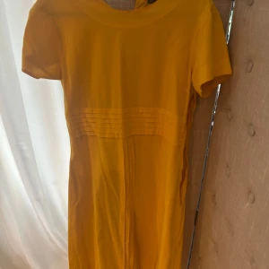 Gul kortärmad klänning från Gap - Snygg gul klänning från Gap med korta ärmar och rund hals. Klänningen har dekorativa horisontella sömmar i midjan som ger en cool detalj. Tillverkad i bomull, perfekt för varma dagar och enkel att styla med sneakers eller sandaler.