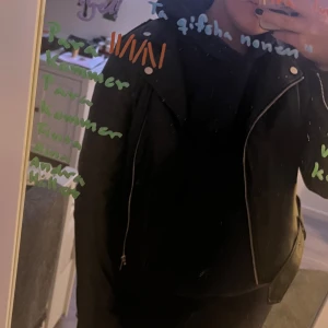 Svart skinnjacka med dragkedjor - Säljer en svart skinnjacka med coola silverfärgade dragkedjor och detaljer. Jackan har klassisk bikerstil med snedställd dragkedja framtill, bred krage och dragkedjor vid ärmsluten. Perfekt för dig som vill ha en edgy look. Jackan har använts mycket och har spruckit i innertyget vid ryggen (se sista bilden). Detta är dock inget som påverkar användningen och syns inte utifrån! 