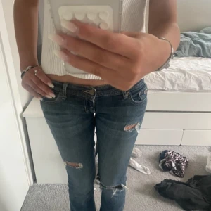 Blå bootcut hollister jeans med slitningar - Säljer ett par blå bootcut  jeans med snygga slitningar på låret och knät. Låg midja och klassiska bakfickor med dekorativa sömmar. Jeansen har en normal passform och är tillverkade i denim med lite stretch för extra komfort. Midja 36 innerben 84