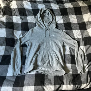 Grå hoodie från Nike med huva - Säljer en stilren grå hoodie från Nike med klassisk logga på bröstet. Tröjan har huva med snörning, magficka och långa ärmar. Perfekt för chill dagar eller när du vill ha en enkel och snygg look.