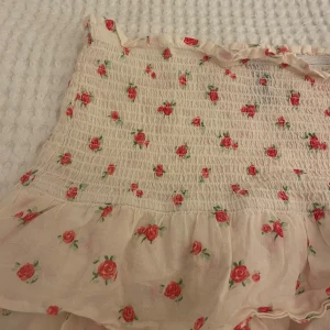 Blommig volangkjol från hm Divided - Supersöt kort kjol från hm Divided i ljusbeige med små röda rosor och gröna blad. Perfekt för varma dagar och ger en riktigt somrig känsla.💞💞