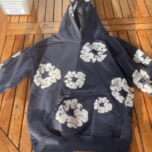 mörkblå hoodie från Denim Tears med tryck - Cool mörkblå hoodie från Denim Tears med unika vita blomliknande tryck över hela tröjan. Klassisk känguruficka framtill och huva. Perfekt för dig som vill sticka ut med streetwear vibes.