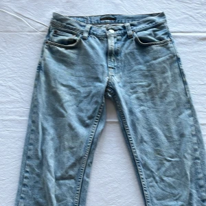 Ljusblå jeans från Nudie Jeans - Säljer ett par klassiska ljusblå jeans från Nudie Jeans med fem fickor och raka ben. Jeansen har en snygg tvätt och subtila kontrastsömmar, samt Nudie-logga på bakfickan. Perfekta för dig som gillar en avslappnad och tidlös stil. Gritty Jackson 