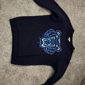 Mörkblå Kenzo tröja med tigertryck - Snygg mörkblå långärmad tröja från Kenzo med ikoniskt tigertryck i blå toner och texten Kenzo Paris framtill. Köpt för 1000 kr pris kan diskuteras👍