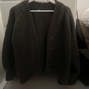 Mörkgrön stickad kofta med knappar - Säljer en mysig mörkgrön stickad kofta med stora knappar framtill. Koftan har en ribbad struktur och långa ärmar, perfekt för kyliga dagar. Den har en klassisk design som passar till många olika stilar.