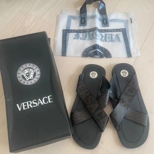 Versace Tofflor  - Versace tofflor i väldigt fint skick, där påse och box ingår. Däremot är boxen lite trasig. Ordinarie pris över 5000kr. 