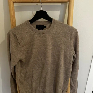 Beige merinoulltröja från Riley - Säljer en stilren beige tröja från Riley i mjuk merinoull. Tröjan har rund halsringning och långa ärmar, perfekt för lager-på-lager under kyliga dagar. Enkel och klassisk design som funkar till allt. Den är ursprungligen i storlek S men krymptes i maskinen så passar nu XS