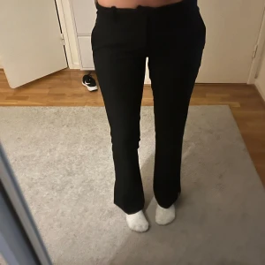 Svarta bootcut kostymbyxor med slits - Snygga svarta kostymbyxor med bootcut passform och slits nertill vid benslut. Byxorna har låg  midja och klassisk look med fickor bak. Perfekta för dig som gillar stilrena och trendiga byxor med en twist.