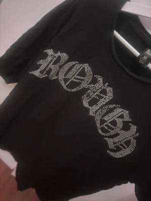 Svart t-shirt med strass från Black Squad - Svart t-shirt från Black Squad i relaxed fit med coolt strassmönster i form av texten 'ROUGH' på bröstet. Klassisk rund halsringning och korta ärmar. 