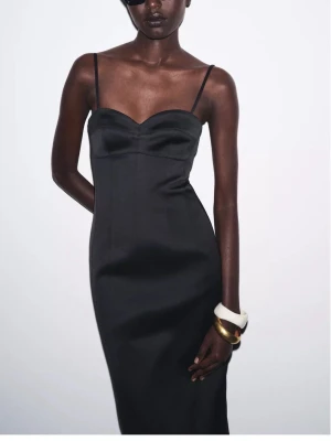 Svart satinklänning med smala axelband - Supersnygg svart klänning i satin med smala axelband och hjärtformad urringning. Klänningen är figurnära och har en klassisk, elegant siluett som slutar strax under knäet. Helt oanvänd. Original pris 699kr säljer för 150kr.