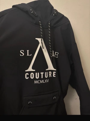 Slade skidjacka  - Säljer en svart jacka från Slade Couture med stor vit logga framtill och snörning i huvan. Jackan  har en praktisk ficka med knappar på magen och coola detaljer på snörena. Perfekt för dig att åka slalom/skidor+ annat