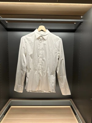 Vit skjorta från Riley - Klassisk vit skjorta från Riley i bomull med lång ärm och knappar framtill. Skjortan har en stilren krage och enkel design som passar till många olika looks. Perfekt för dig som gillar en clean och tidlös stil.