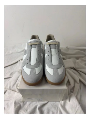 Maison margiela sneakers. - Säljer ett par stilrena sneakers i vitt och ljusgrått med snygga mockadetaljer och klassisk gummisula. Skorna har snörning och en låg profil som passar perfekt till jeans eller shorts. Materialmix av skinn och mocka ger en clean och modern look.