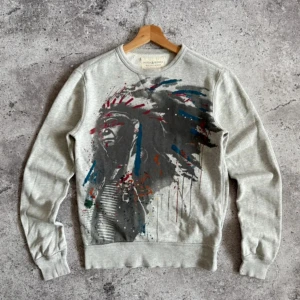 Grå sweatshirt från Ralph Lauren XS - Snygg grå sweatshirt från Denim & Supply Ralph Lauren i storlek XS. Framsidan har ett coolt färgstänksmotiv i blått, rött och svart. Tröjan har rund hals, ribbade muddar och lång ärm. Perfekt för dig som gillar streetstyle och konstnärliga prints.