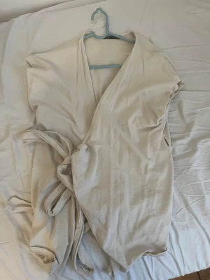Beige omlotttopp från Zara - Säljer en beige omlotttopp från Zara i mjukt tyg. Toppen har korta ärmar, knytband i midjan och v-ringad hals. Perfekt för en chill och stilren look. Tror inte den säljs längre på Zara
