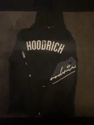 Hoodrich hoodie  - Snygg svart hoodie från Hoodrich, ett populärt streetwear-märke med stark identitet. Kaxig design med stora tryck både fram och bak – bland annat texten “FROM NOTHING TO SOMETHING”, som verkligen sticker ut och ger hoodien en rå, motiverande vibe.  ✔ Bekväm passform ✔ Tjock och skön kvalitet ✔ Stilren svart färg som passar till allt ✔ Perfekt för vardag, streetstyle eller chill