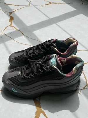 Nike Air Max 95 svart/camo  - Säljer ett par Nike Air Max 95 i svart och grått med turkosa detaljer. Skorna har mesh och skinnpaneler, synlig Air-dämpning och snörning. Insidan har ett camouflagemönster i grönt, beige och vinrött. Perfekta för dig som vill ha något unikt och street.