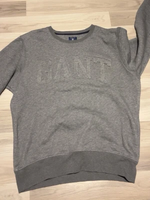 Grå sweatshirt från GANT XL - Säljer en stilren grå sweatshirt från GANT i storlek XL. Tröjan har rund halsringning, diskret broderad GANT-logga framtill och är tillverkad i mjuk bomullsmix. Perfekt för en chill och avslappnad look.