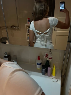 Vit topp med öppen rygg och knyt - Säljer en vit topp i mjukt material med korta ärmar. Toppen har en snygg öppen rygg med knytband som detalj. Perfekt för dig som gillar stilrena plagg med en twist. Passformen är normal och toppen är enkel att matcha till olika outfits. Knuten ska naturligtvis se bättre ut är bara sämst på att knyta haha! Felfritt skick