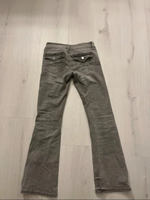 Grå bootcut jeans från Gina Tricot - Säljer ett par grå jeans från Gina Tricot i storlek 158. Byxorna har bootcut-modell, klassiska fickor med lock och knapp bak samt låg midja.
