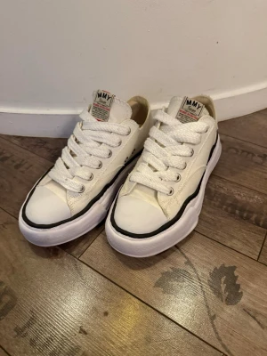 MMY vita - Säljer ett par vita sneakers från MMY med chunky vit sula och svart vågig detalj runt om. Skorna har breda vita snören, rund tå och är gjorda i canvasmaterial. Klassisk låg modell med cool retrovibe och tydlig logga på plösen och hälen. Bra skick. Pris kan diskuteras vid snabbaffär. 
