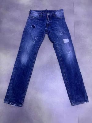 Dsquared2 jeans - Säljer ett par Dsquared²-jeans i blå denim. De har snygga slitningar och lagningar som är typiska för märket och ger byxorna mycket karaktär. Jeansen har använts men är i bra skick – slitningarna är en del av designen. Passar perfekt till både vardag och lite mer uppklädda outfits.  Märke: Dsquared² Färg: Blå Skick: Bra begagnat skick Hör av dig vid frågor 😊