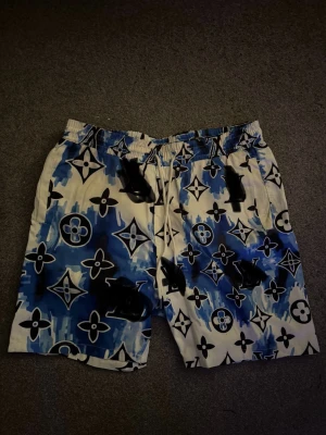 LV swimming shorts! - Säljer ett par riktigt snygga shorts från .med blå och vita toner och ikoniskt monogrammönster. De har elastisk midja med snörning och är tillverkade i ett lätt, syntetiskt material som passar perfekt för sommaren.
