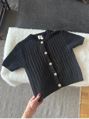 H&M - Svart kabelstickad tröja från HM med guldknappar. Sparsamt använd och i fint skick. Stl  S