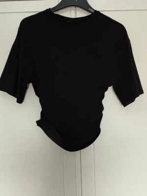 Svart t-shirt med snörning Gina Tricot - Svart T-shirt från Gina tricot, stora ärmar och tajt i midjan jättesnygg använd ett par fåtal gånger 