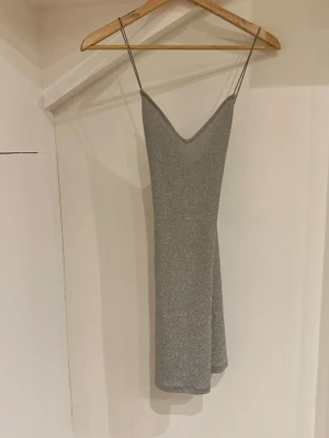 Glittrig silver kortklänning H&M XS - Säljer en glittrig silverfärgad kortklänning från H&M:s DIVIDED-kollektion i storlek XS. Klänningen har tunna axelband, v-ringning, och korsad rygg perfekt för dig som vill sticka ut. Materialet är mjukt och stretchigt syntet med glittereffekt.