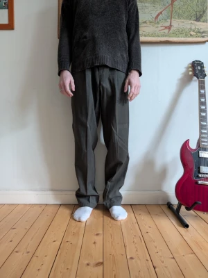 Mörkgröna kostymbyxor med rak passform - Säljer ett par mörkgrå kostymbyxor med klassisk rak passform. Byxorna har pressveck och sitter snyggt i midjan. Perfekta för dig som gillar en stilren och enkel look. Materialet känns mjukt och är troligtvis bomull eller polyester.