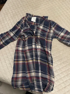 Rutig skjorta från H&M L.O.G.G. - Säljer en långärmad rutig skjorta från H&M L.O.G.G. i marinblått, vinrött, vitt och gult. Skjortan har klassisk krage, knappar framtill och är gjord i mjuk bomull. Perfekt för dig som gillar avslappnad och tidlös stil.